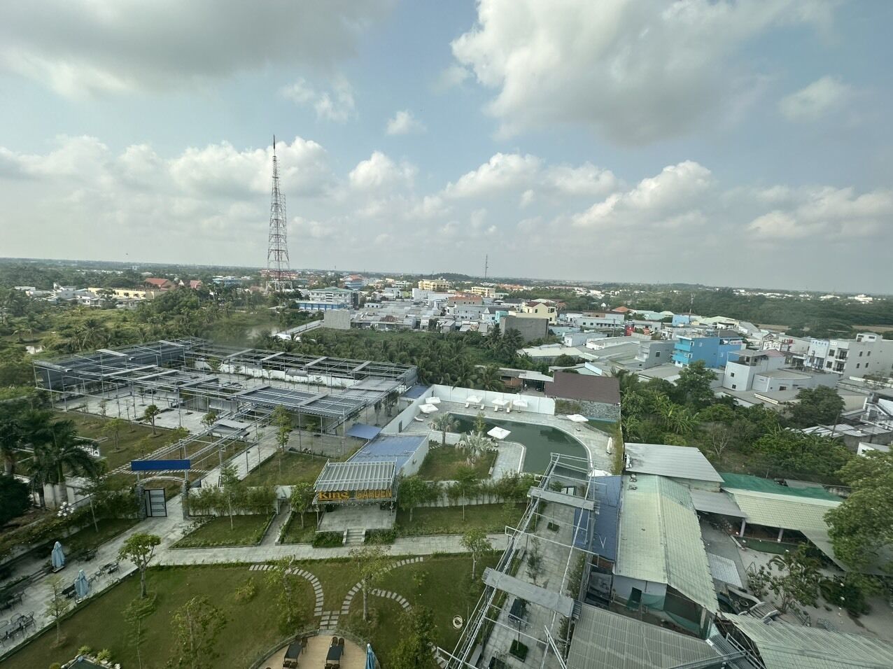 An aerial view of a cityscape with a mix of residential and commercial buildings, a prominent tower, and a large open area with greenery and a pool.