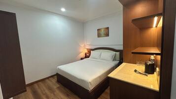 Un dormitorio con cama, mesita de noche, lámpara y un estante con objetos.