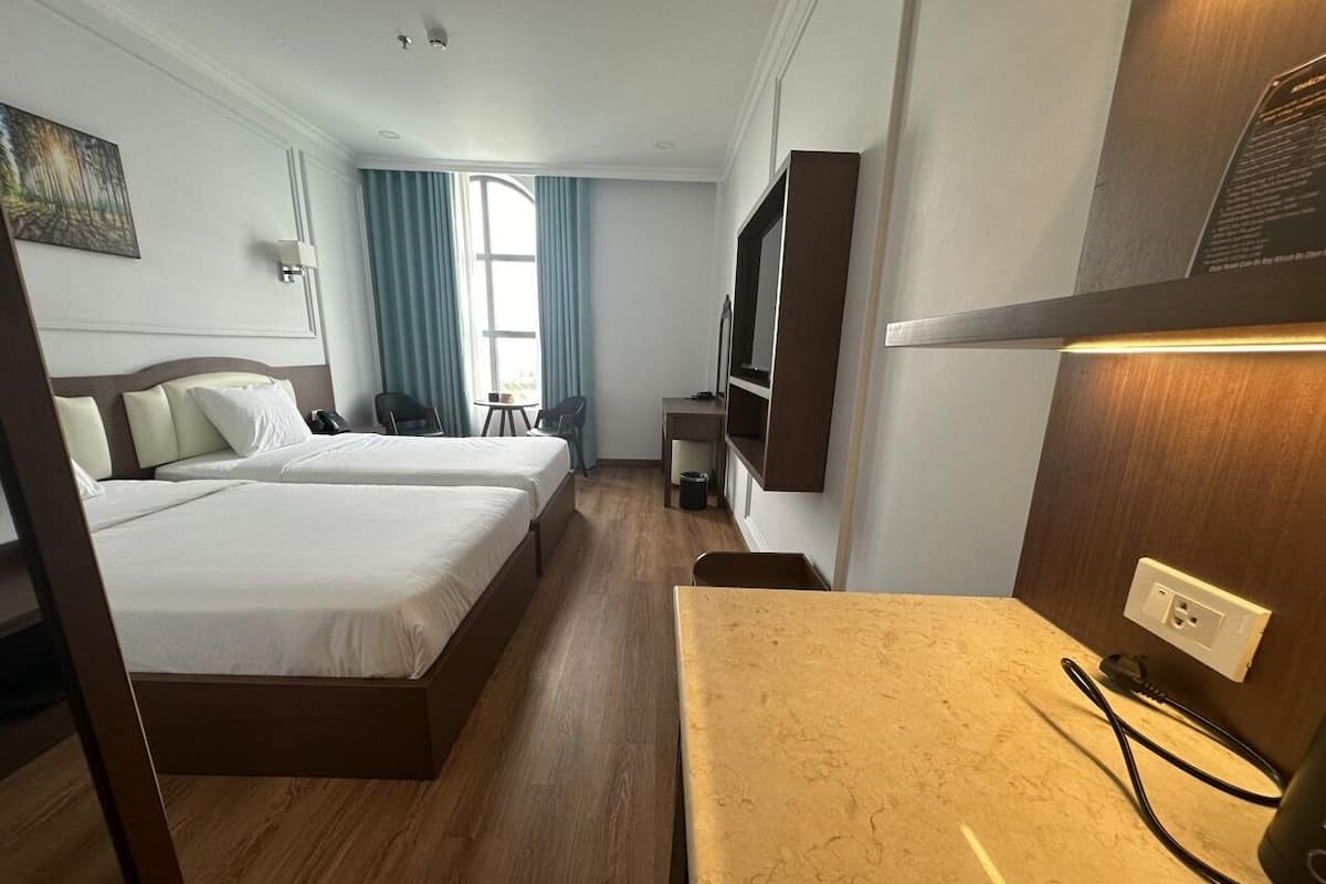 A hotel room with two beds, a desk, a TV, and a window with curtains.