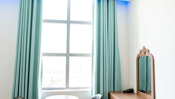 A room with a wooden desk, two chairs, a round table, a mirror, and teal curtains.
