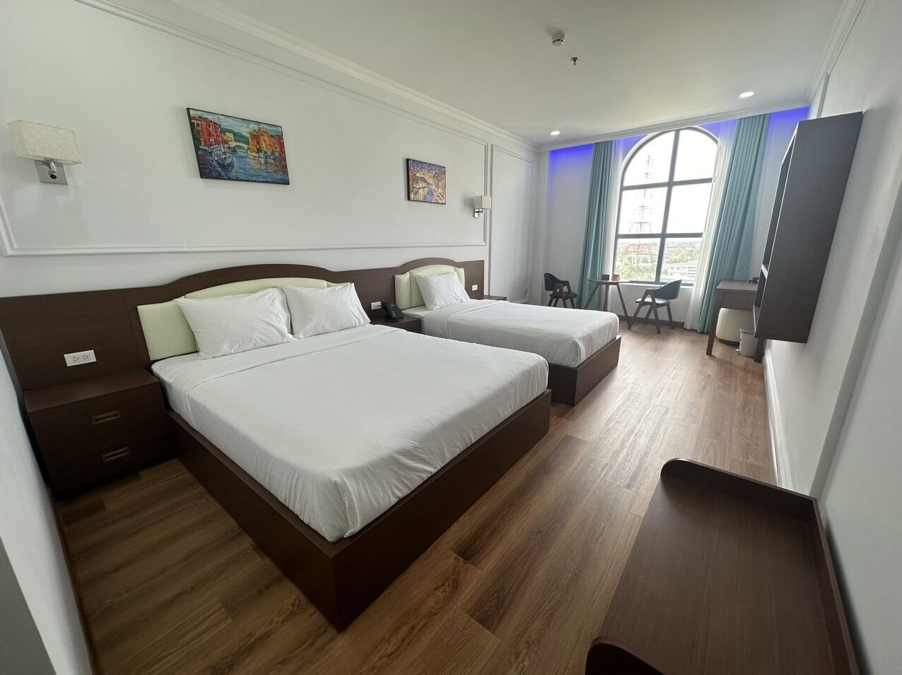 A hotel room with two beds, a desk, a chair, and a large window with curtains.