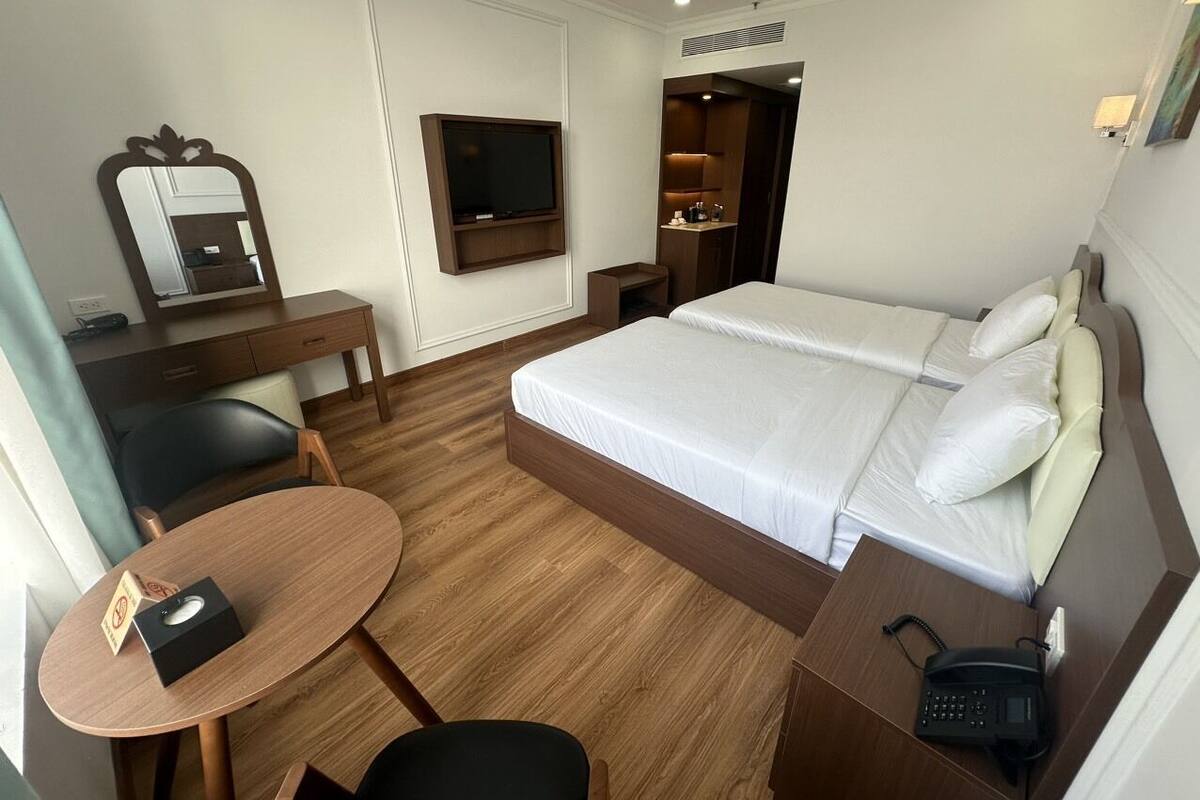 A hotel room with a bed, a desk, a chair, a TV, and a small table.