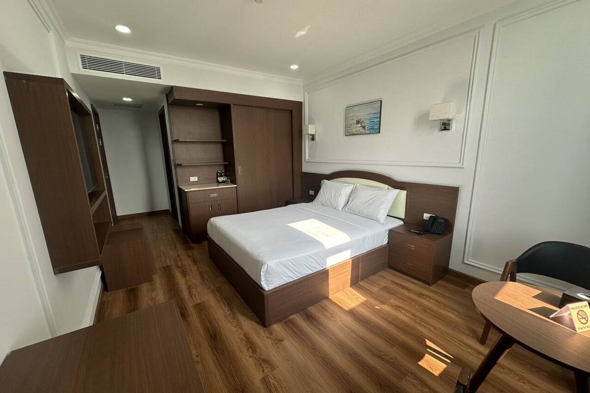 A hotel room with a bed, bedside table, and a desk with a chair.