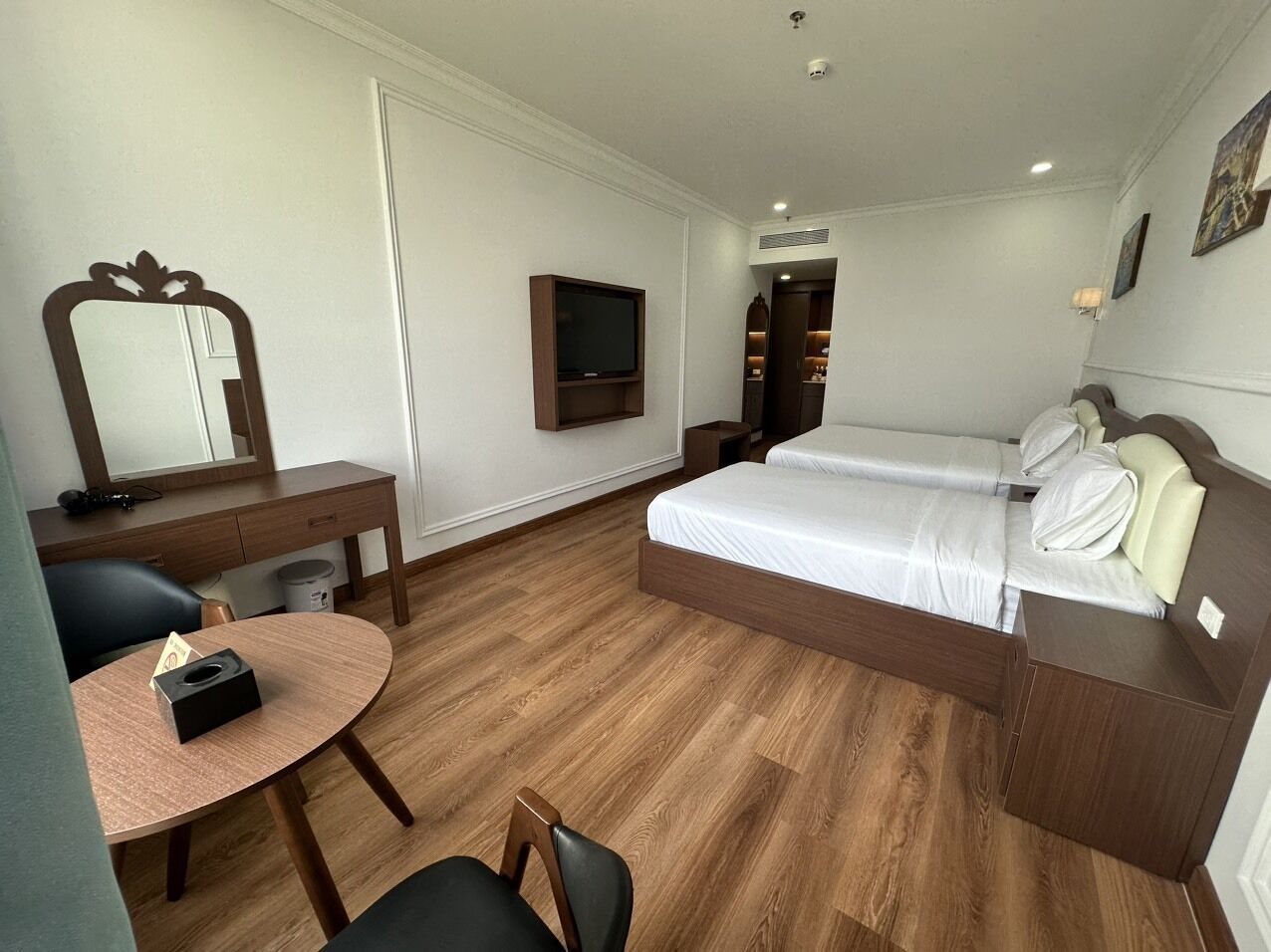 A hotel room with a bed, a desk, a chair, a TV, and a mirror.