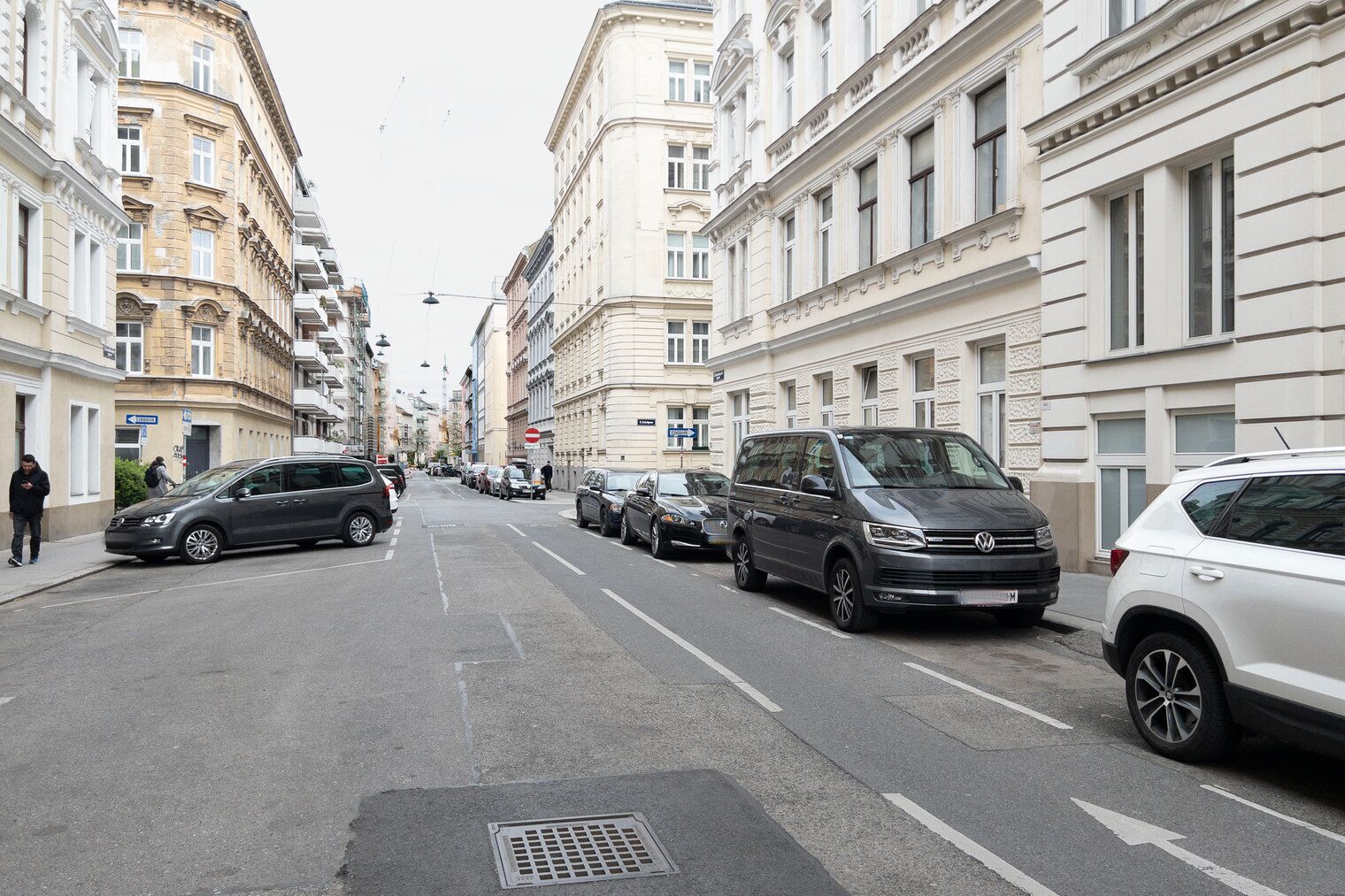 Una calle flanqueada por edificios de varios pisos, automóviles estacionados y un peatón.