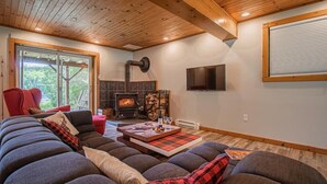 A cozy living room with a fireplace, a large sofa, and a television. - Peaceful Chalet on Pristine Lac de l'Abies in Labelle, QC. Dogs Welcome! (Labelle)