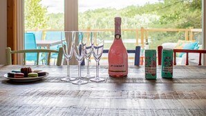 A table with a bottle of JP Chenet champagne, four glasses, and two cans of Fanta Grape on a wooden table with a view of greenery outside. - Peaceful Chalet on Pristine Lac de l'Abies in Labelle, QC. Dogs Welcome! (Labelle)