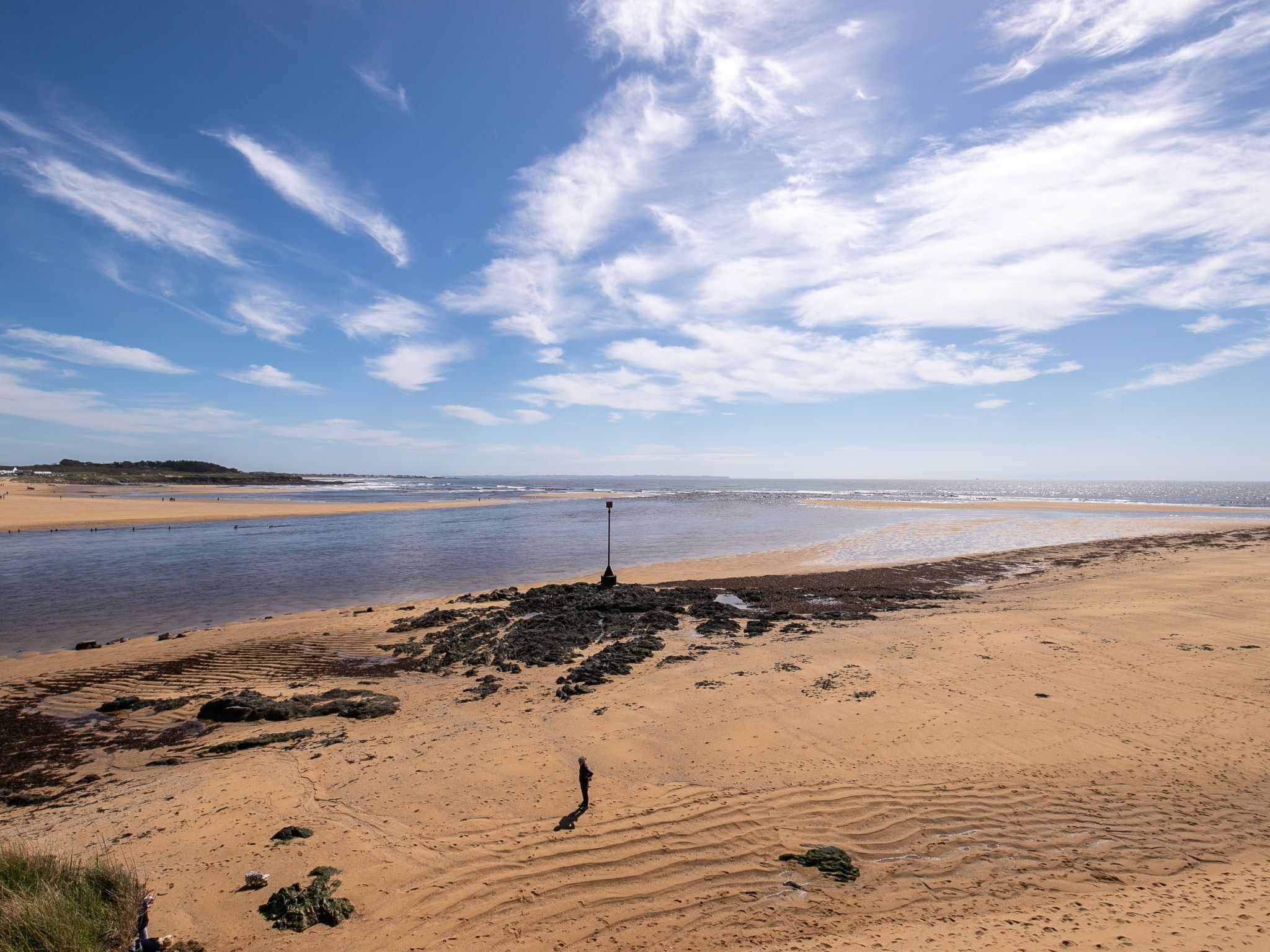 A beach with a clear sky, sandy shore, and a rocky outcrop.