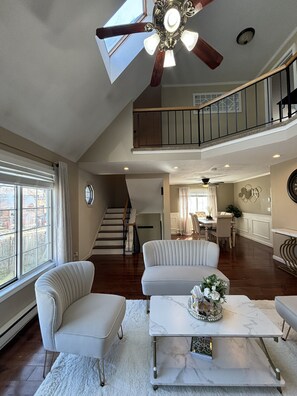 A spacious living area with a high ceiling fan, a staircase to an upper level, and a dining area with a view of the outdoors. - Home Away from Home! (Worcester)