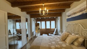 A bedroom with a wooden ceiling, a bed with a patterned bedspread, a chandelier, and a view of a balcony with chairs. - Casa Moises Bimenes (Las Cruces)