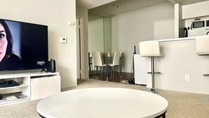 Ein modernes Wohnzimmer mit Flachbildfernseher, rundem Tisch und Essbereich mit Stühlen.