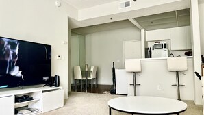 Ein modernes Wohnzimmer mit Flachbildfernseher, rundem Couchtisch und Essbereich mit Stühlen und Glastisch.