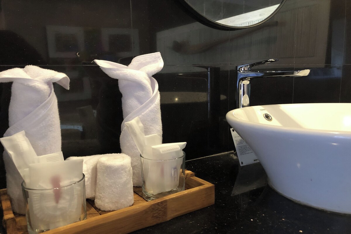 A bathroom with a white sink, a mirror, and a wooden tray holding white towels and a glass container with a toothbrush.