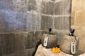 Un baño con baldosas de piedra y dos dispensadores de jabón y champú, identificados como 