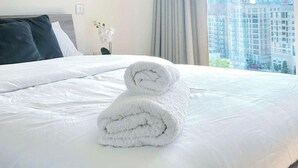 A neatly made bed with white linens and a rolled towel on the bed.