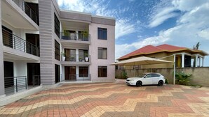 A multi-story building with balconies, a car parked in front, and a patterned pavement. - Charming 2-Bed Apartment in Kigali (Kigali)