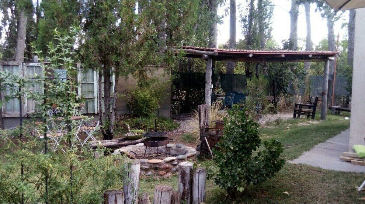A backyard with a wooden pergola, a fire pit, and a small garden area with various plants and a bench.