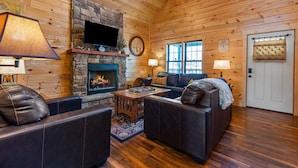 Ein gemütliches Blockhaus-Interieur mit Kamin aus Stein, Ledersofas und Holzdielen.