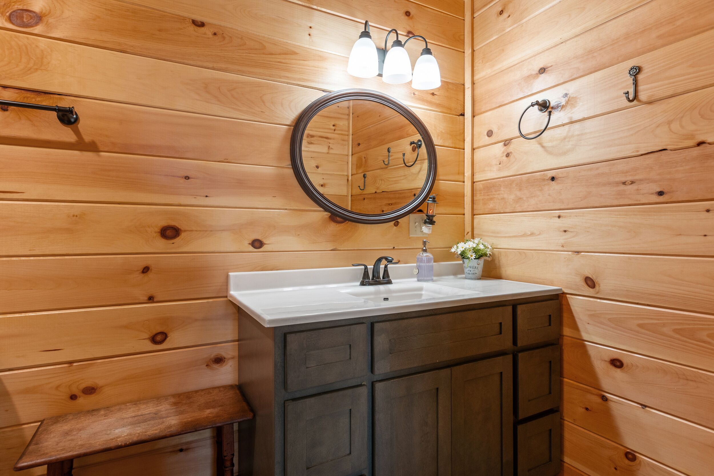 A wooden-paneled bathroom with a round mirror, a sink, and a bench.