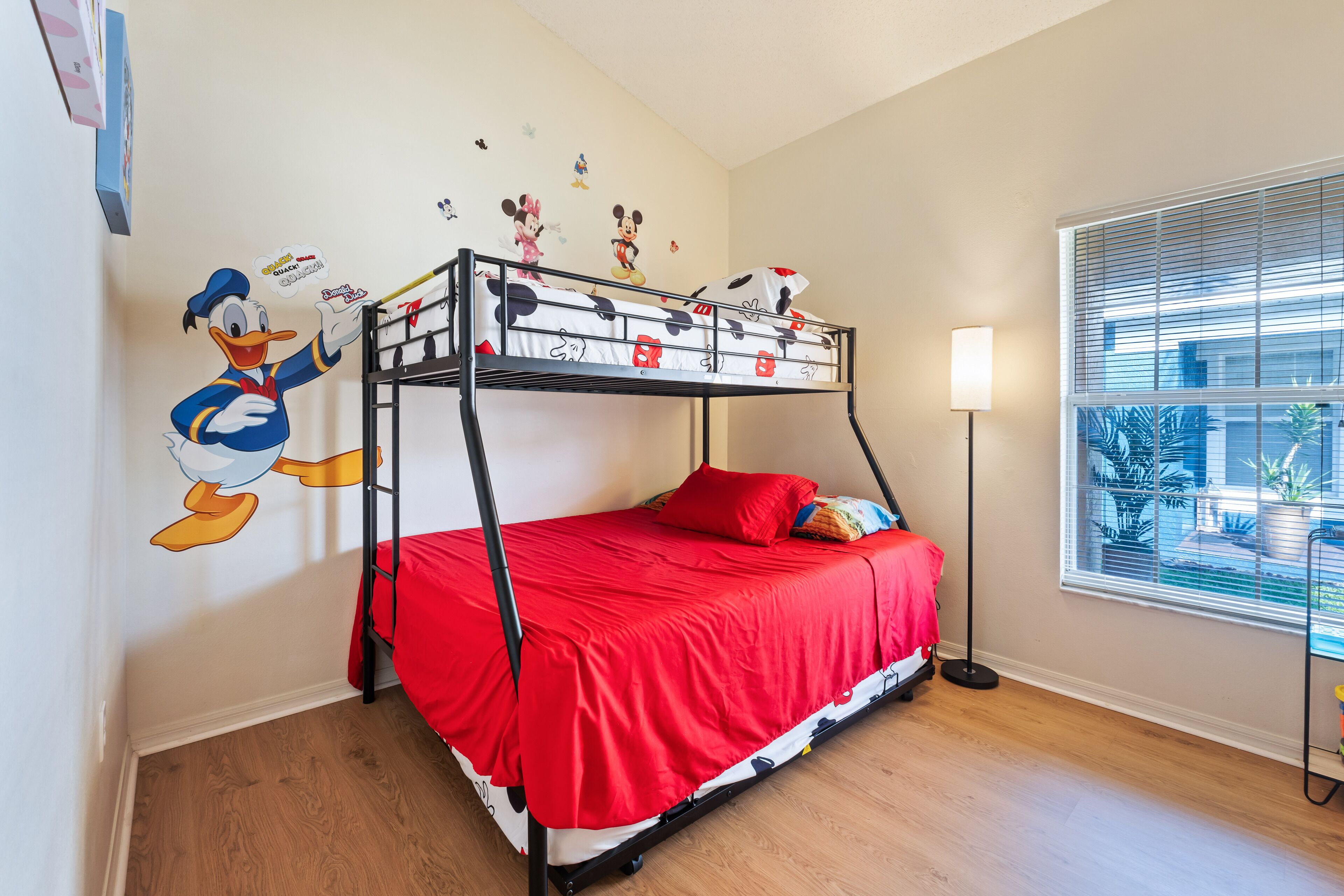 Ein Etagenbett mit roter Bettdecke, einer Wandsticker mit Mickey Mouse und einer Lampe in der Nähe eines Fensters.