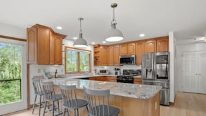 A modern kitchen with wooden cabinets, stainless steel appliances, and a large island with bar stools. - Family Luxury: 5BR, Beach, Kayaks, GameRm, Arcade, MovieRm, PingPong, Fire Pit (Saint Leonard)