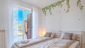 Een slaapkamer met een bed, gordijnen, uitzicht door het raam en een wand met beplanting.