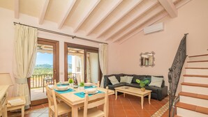 A dining area with a table set for four, a sofa, a small table with a plant, and a staircase. - CDT Cala Del Faro, Porto Cervo, Italy (Porto Cervo)