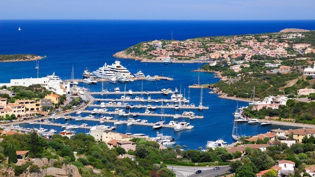 A marina with numerous boats docked, surrounded by residential buildings and greenery. - CDT Cala Del Faro, Porto Cervo, Italy (Porto Cervo)