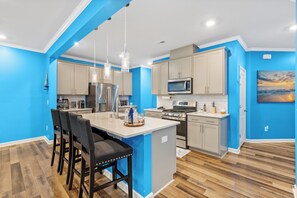 Una cocina moderna con paredes azules, piso de madera y una isla central con taburetes de bar.