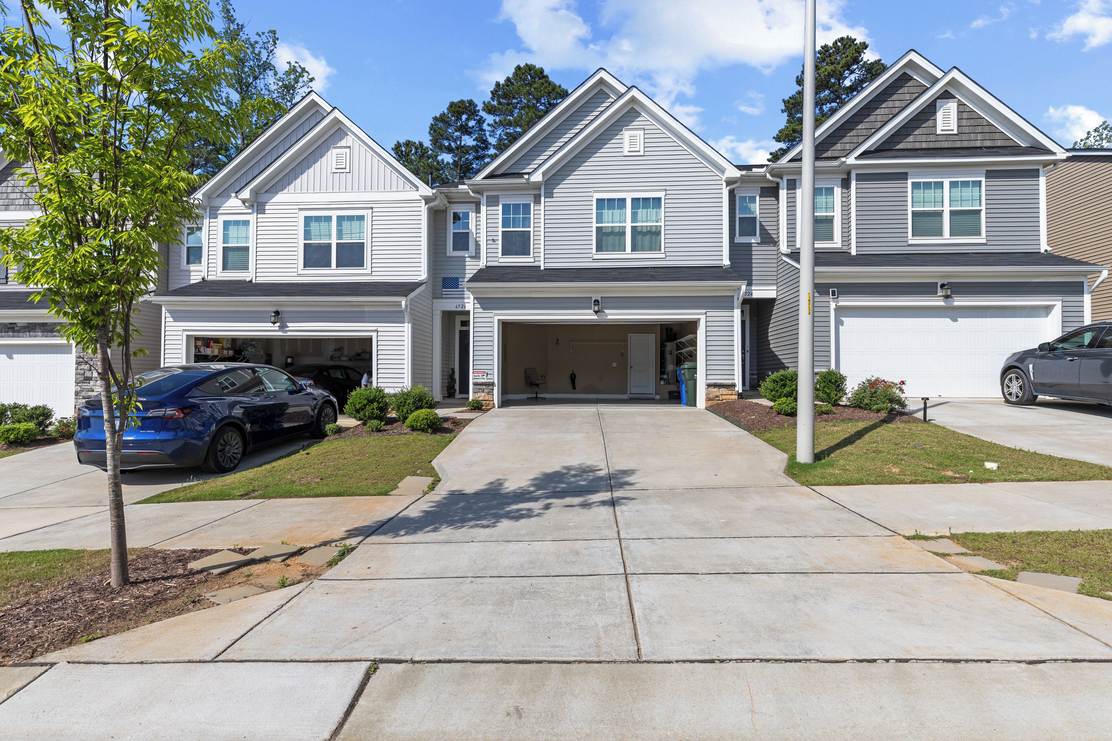 A two-story residential building with a garage, a driveway, and a tree in the front yard.