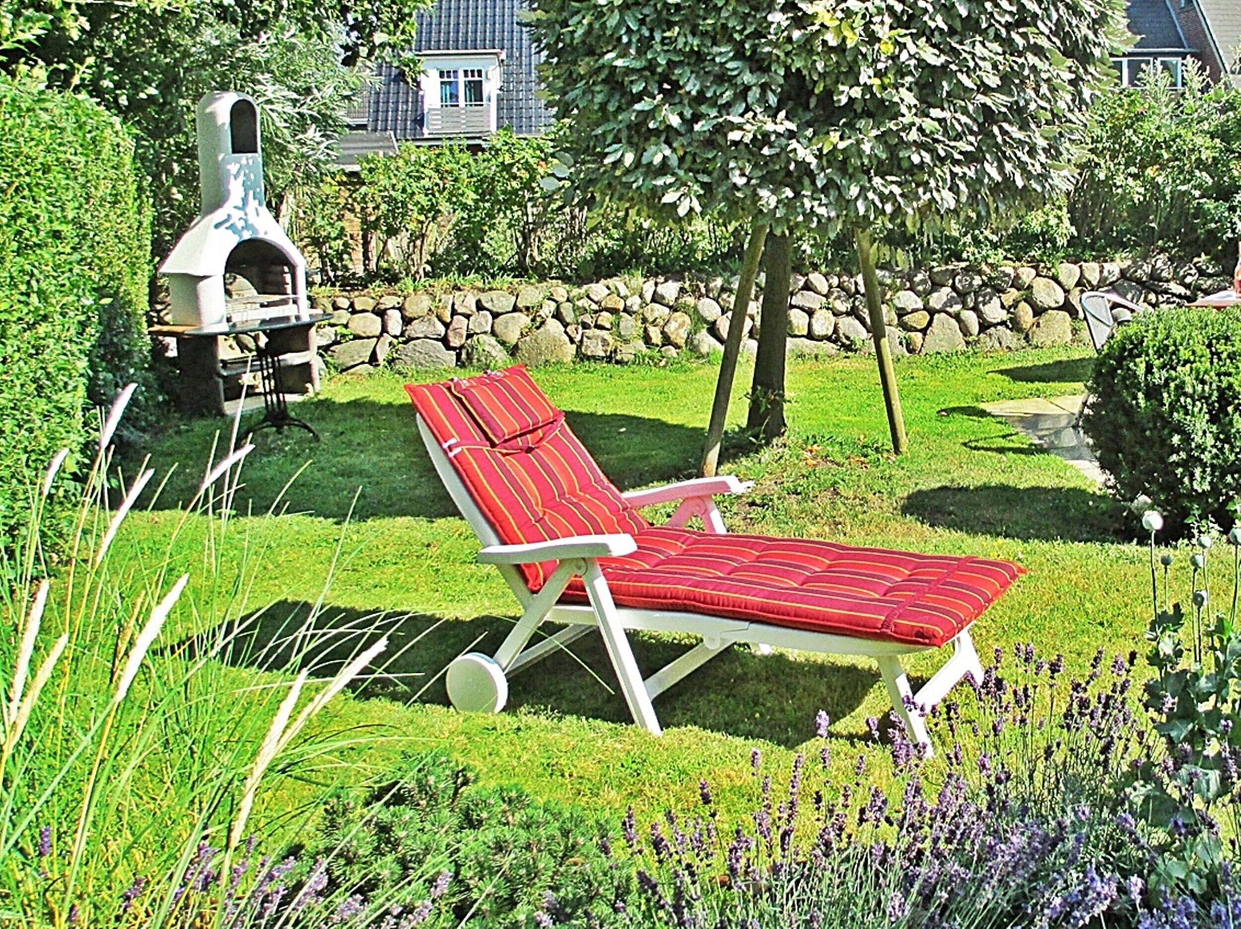 Un jardin avec un fauteuil de relaxation rouge, un mur en pierre et une cheminée.