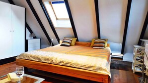 A bedroom with a sloped ceiling, a bed with striped bedding, a bedside table, a chair, and a small table with a glass. - Beautiful Maisonette Apartment with Wi-Fi, Garden and Terrace; Parking Available (Sylt)