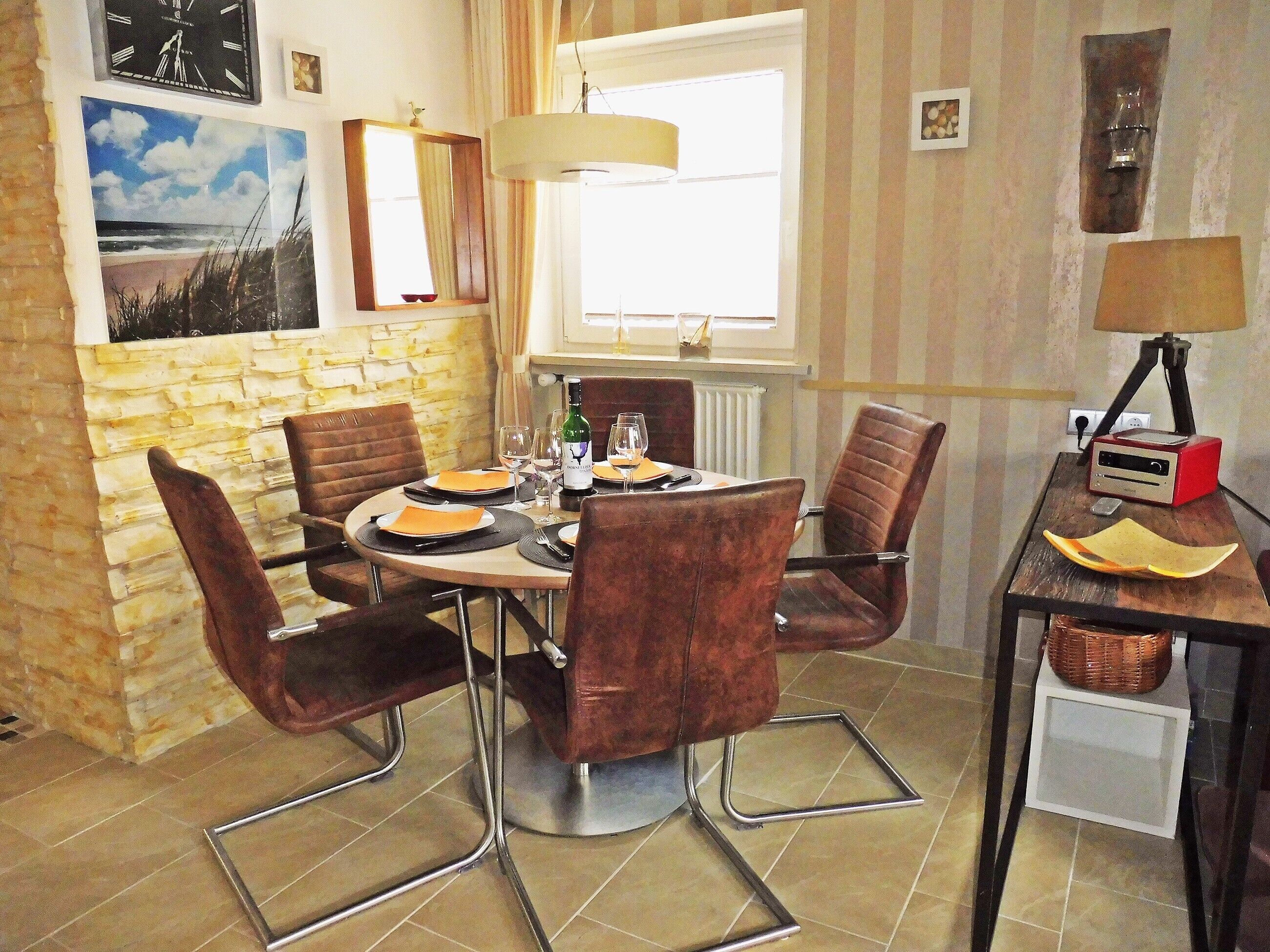 A dining area with a round table, brown chairs, a lamp, and a radio on a side table.