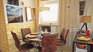 A dining area with a round table, brown chairs, a lamp, and a radio on a side table. - Beautiful Maisonette Apartment with Wi-Fi, Garden and Terrace; Parking Available (Sylt)