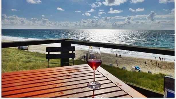 A beach view from a deck with a glass of red wine. - Beautiful Maisonette Apartment with Wi-Fi, Garden and Terrace; Parking Available (Sylt)