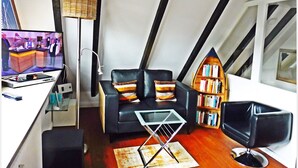 A compact living space with a television, a sofa, a small table, a bookshelf, and a chair. - Beautiful Maisonette Apartment with Wi-Fi, Garden and Terrace; Parking Available (Sylt)