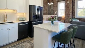 A modern kitchen with white cabinets, a black refrigerator, and a large island with bar stools. - Loft Apartment On Main - Sleeps 4 (Du Quoin)