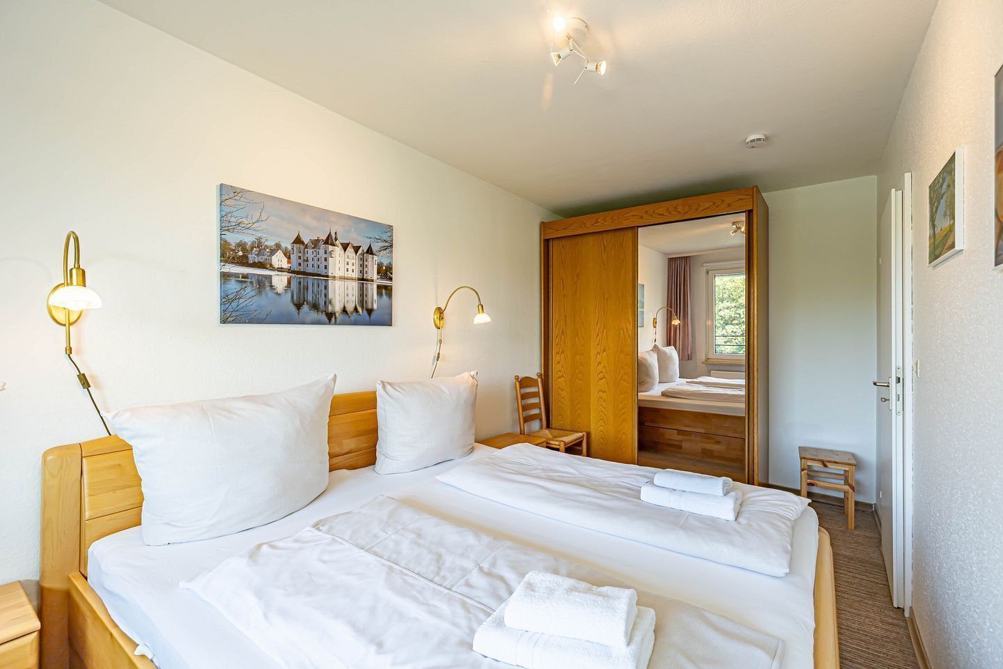 A hotel room with a large bed, bedside lamps, a painting, a mirror, and a window.