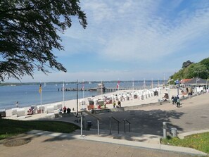En strandpromenad med sittplatser, en brygga som sträcker sig ut i vattnet och flaggor.