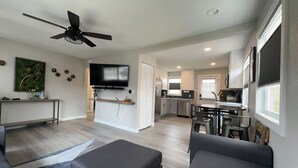 A modern living room with a flat-screen TV, a ceiling fan, and a dining area with a kitchen in the background. - Beautiful, Modern, Quiet, Comfy & Private with a Big Back Yard - 30+ day stays  (Denver)