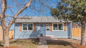 A single-story house with a blue door, white-framed windows, and a small porch. - Beautiful, Modern, Quiet, Comfy & Private with a Big Back Yard - 30+ day stays  (Denver)