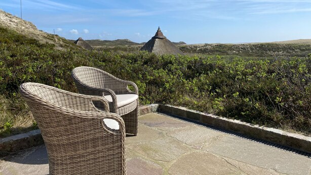 Des chaises en osier sont disposées sur un patio en pierre, offrant une vue sur un paysage caractérisé par des formations rocheuses remarquables.