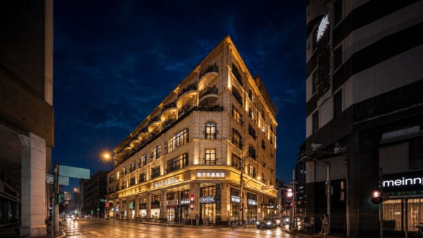 Un hotel de varios pisos con letreros iluminados, una calle mojada y edificios circundantes.