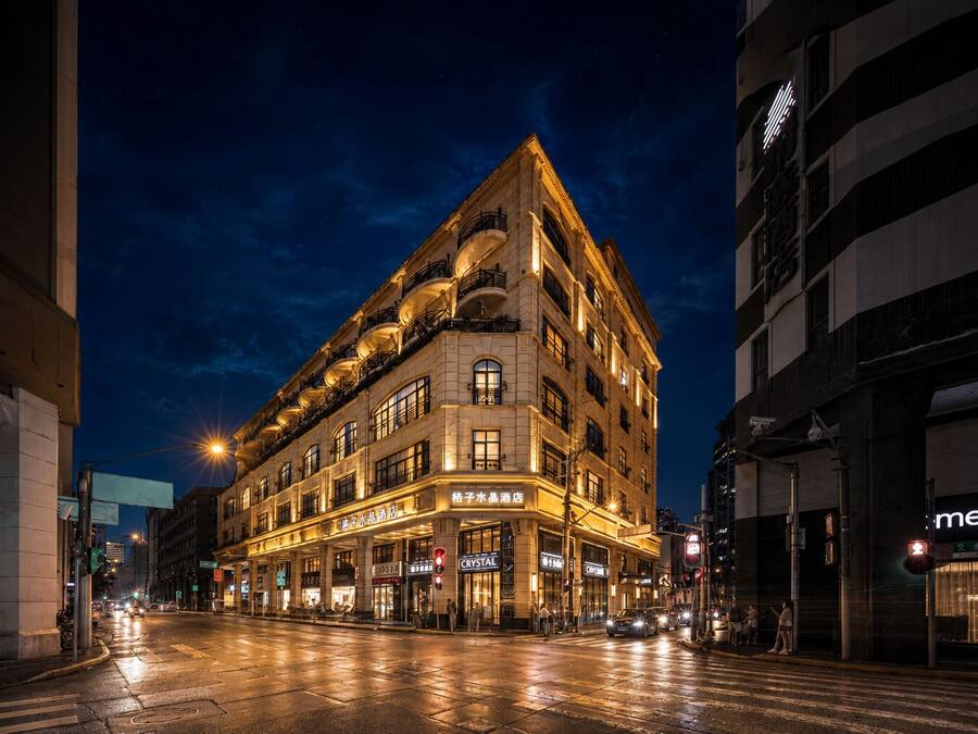 Um hotel de vários andares com letreiros iluminados, rua molhada e edifícios ao redor.