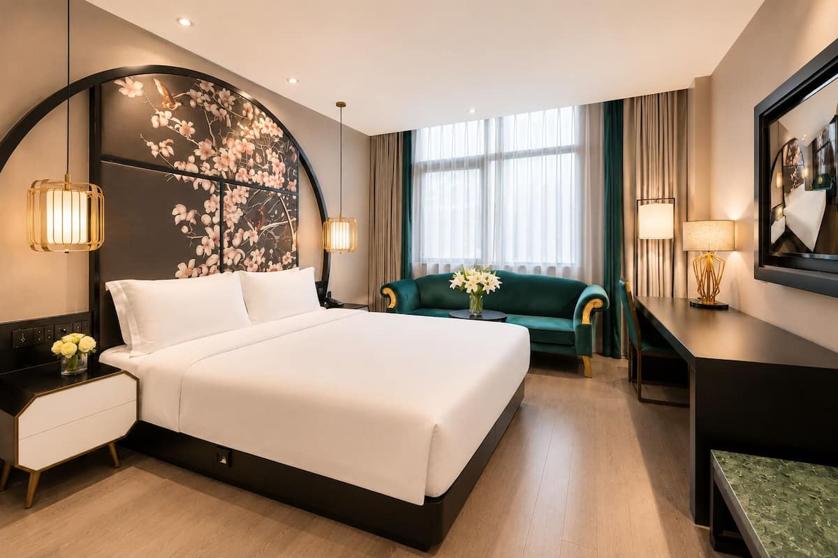 A hotel room with a large bed, a desk, a chair, and a large window with curtains.
