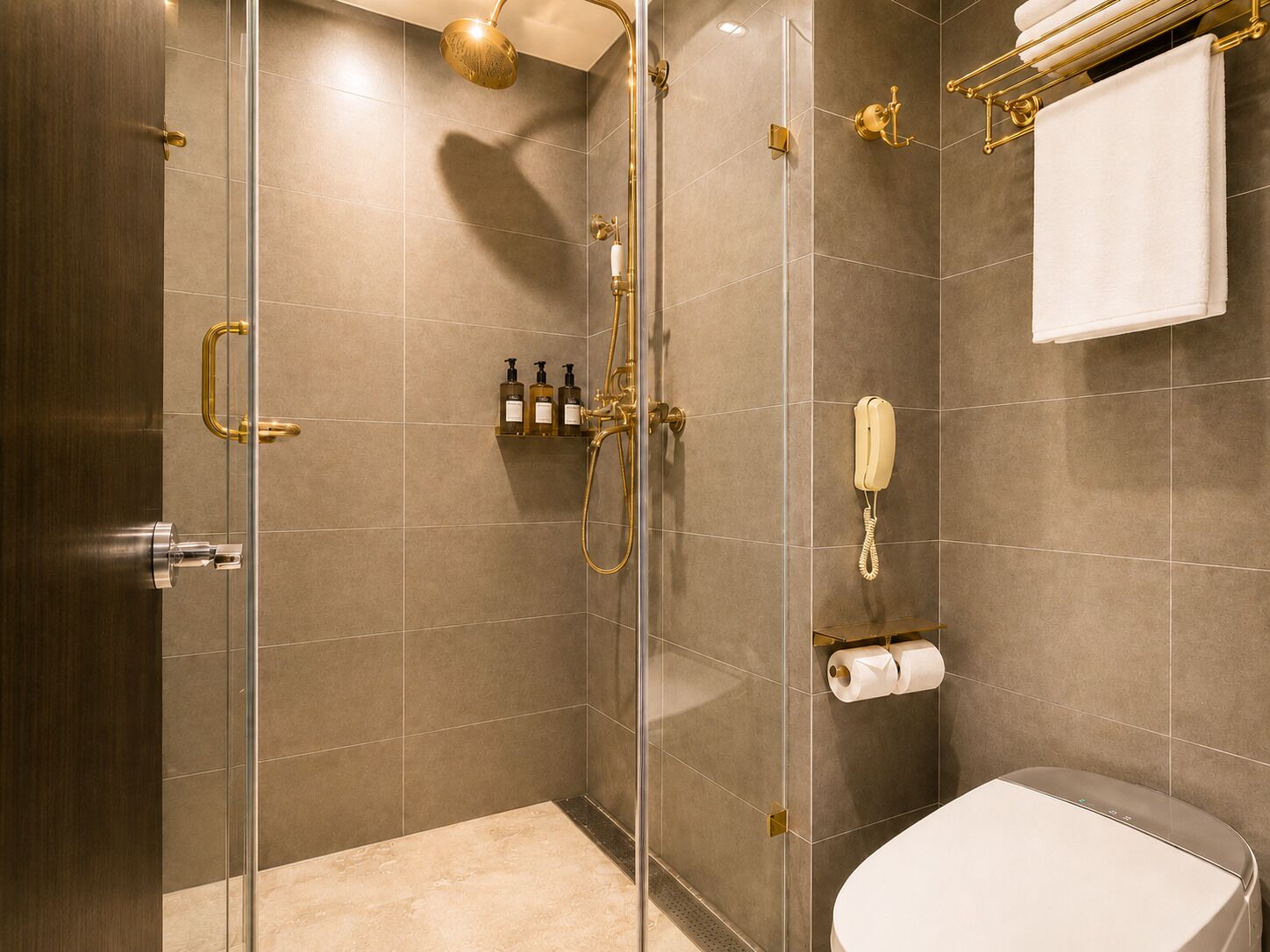 Uma casa de banho moderna com chuveiro de vidro, sanita e porta-toalhas.