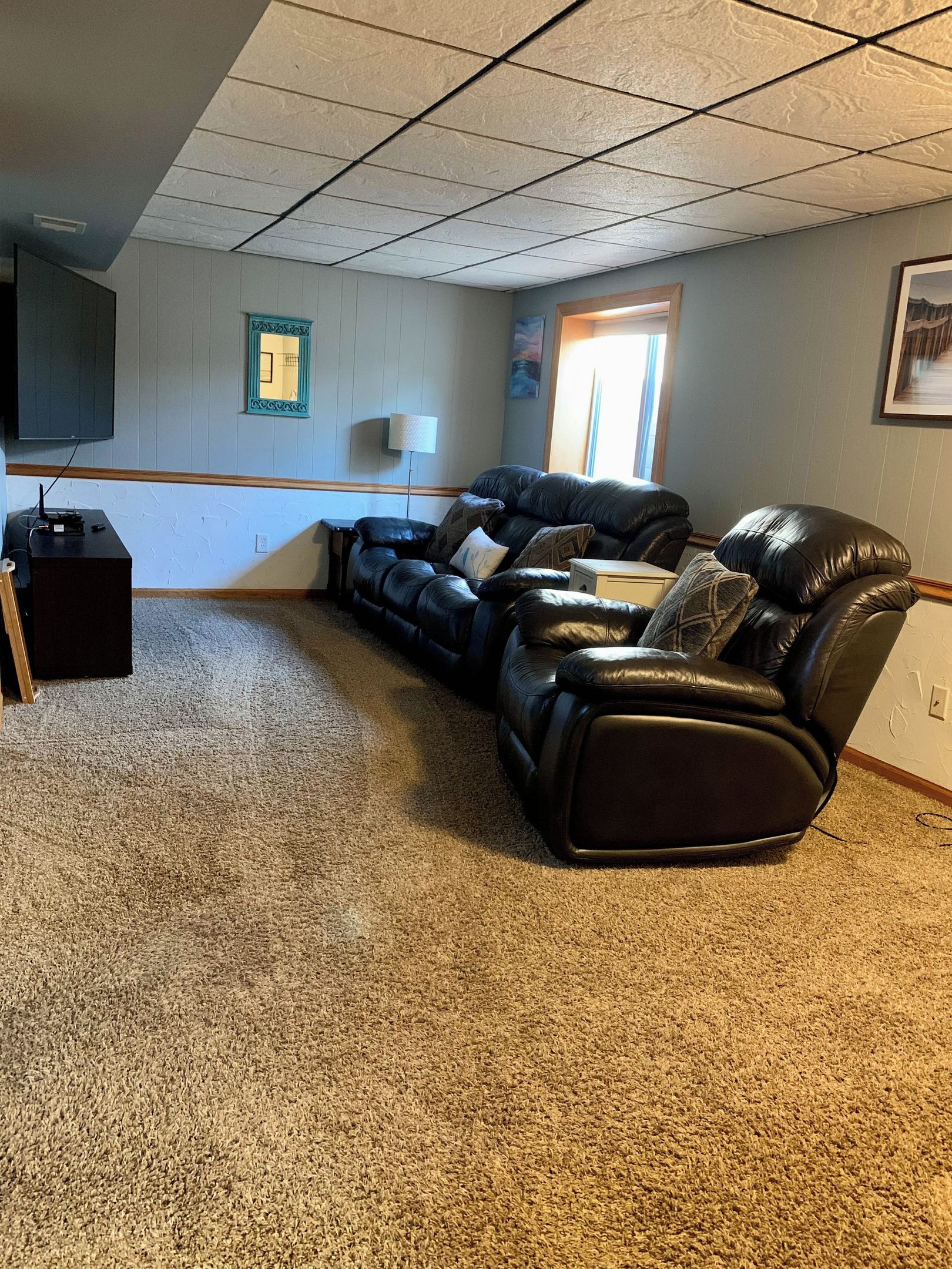 A room with a large black leather sofa, a small table, a lamp, and a painting on the wall.
