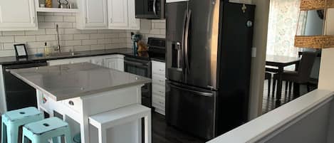 Une cuisine moderne avec des meubles blancs, un réfrigérateur en acier inoxydable et un îlot central doté de tabourets de bar.