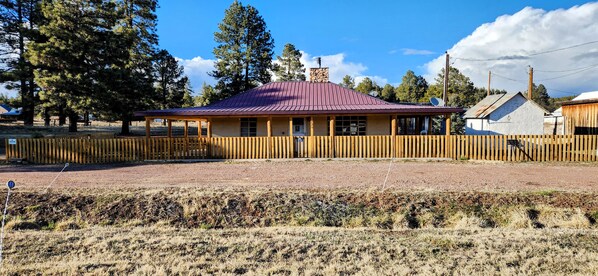 A rustic cabin with a metal roof, wooden porch, and a stone chimney. - Comfortable ranch style cabin with prime location to both Arizona and New Mexico (Luna)