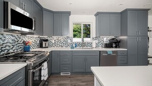 A modern kitchen with grey cabinets, a stainless steel range, and a tiled backsplash. - Updated Spacious Home & Hot Tub (Spokane Valley)